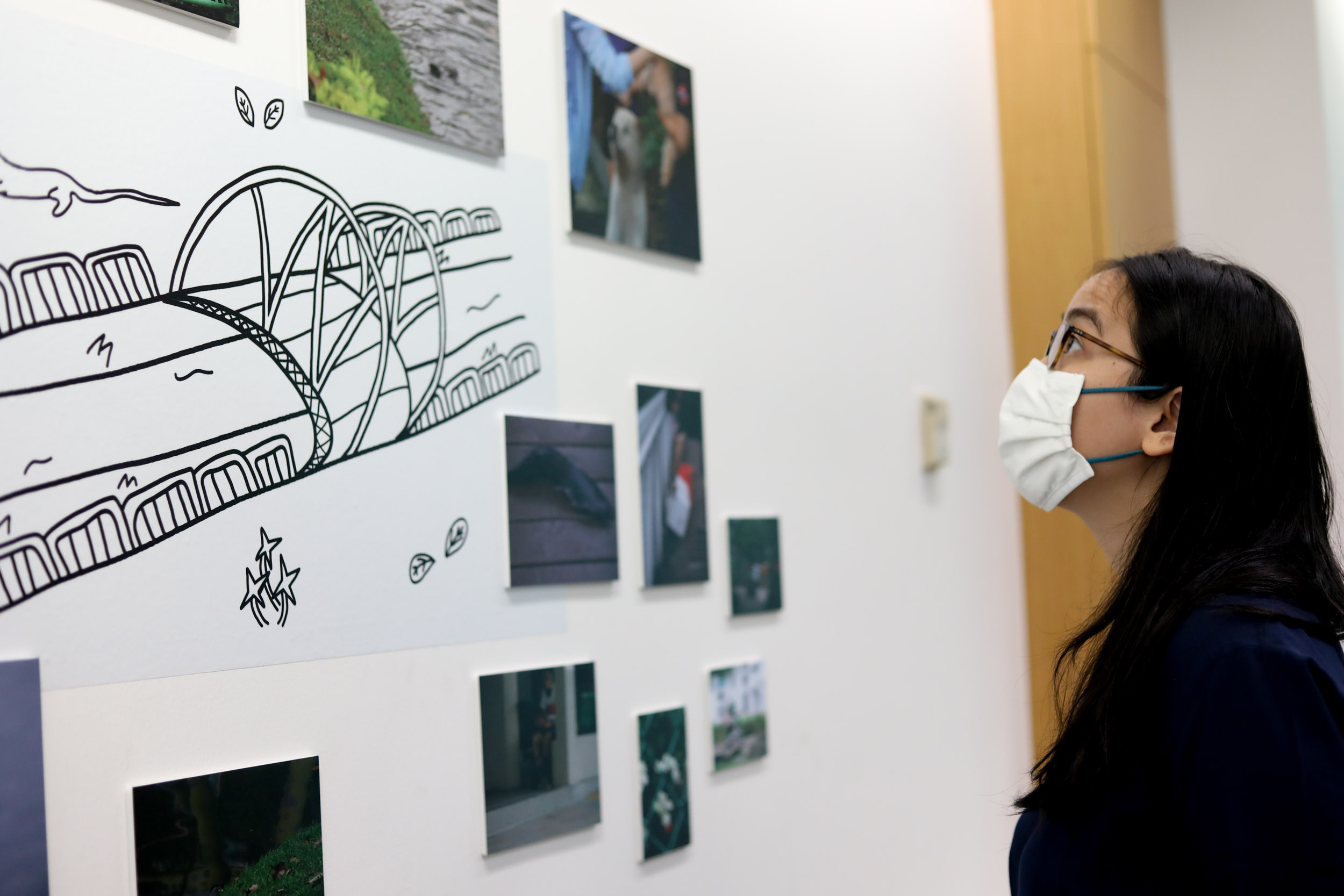 Woman looking at a wall collage of large, medium and small sized photograph arranged around a drawing of a bridge and river