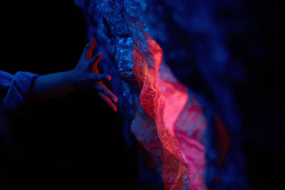 A hand touching a 3d printed panel shaped and textured like a rock. Parts of the panel is glowing red.