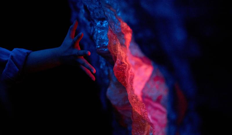 A hand touching a 3d printed panel shaped and textured like a rock. Parts of the panel is glowing red.